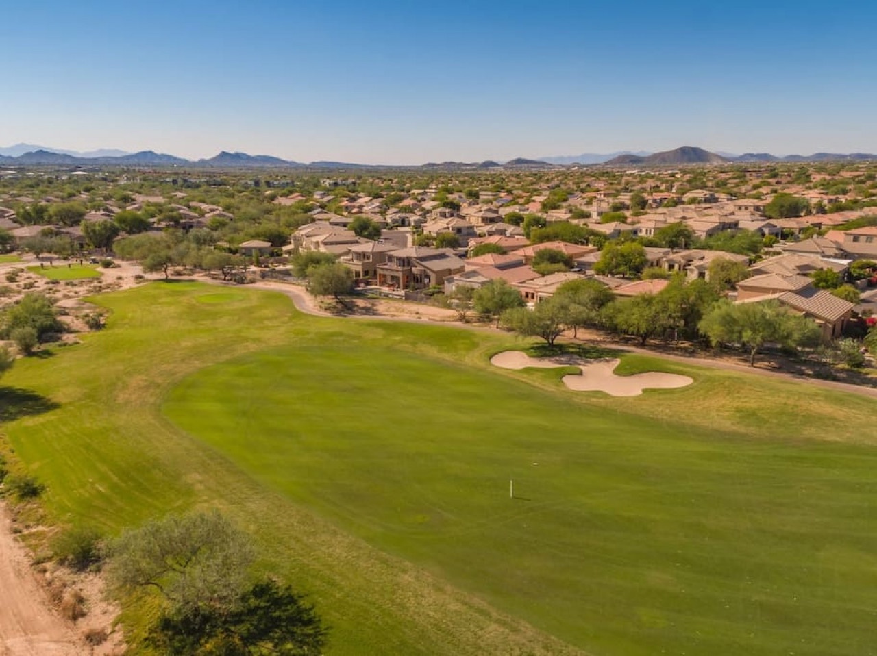Aerial view of pristine golf course fairways surrounded by desert homes with mountain vistas stretching across the horizon.