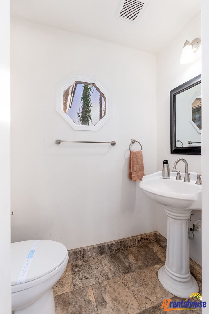 Refresh in your bright, spotless powder room with a classic pedestal sink and charming octagonal window framing a peaceful courtyard view.