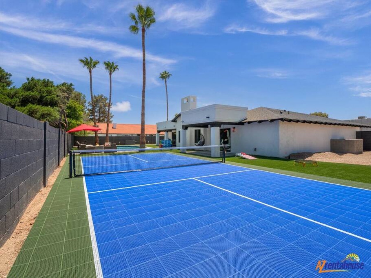 Modern luxury villa featuring a private tennis court and pool area surrounded by palm trees and desert landscaping.