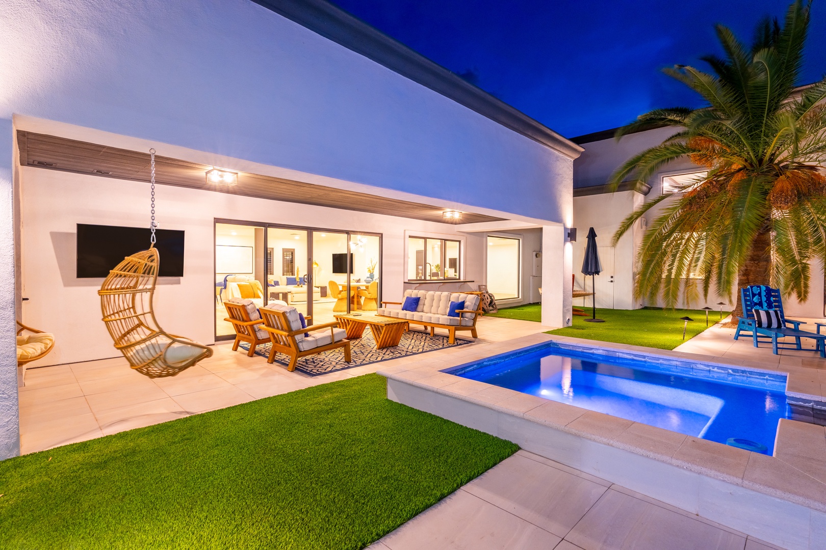 Modern vacation retreat featuring a private pool, covered patio with lounge seating, lush lawn, and swaying palms under a twilight sky.