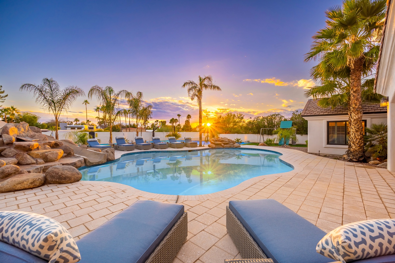 Resort-style oasis bathed in golden sunset light, framing palm trees and a crystalline pool with lounge seating—your perfect desert escape under vibrant skies.
