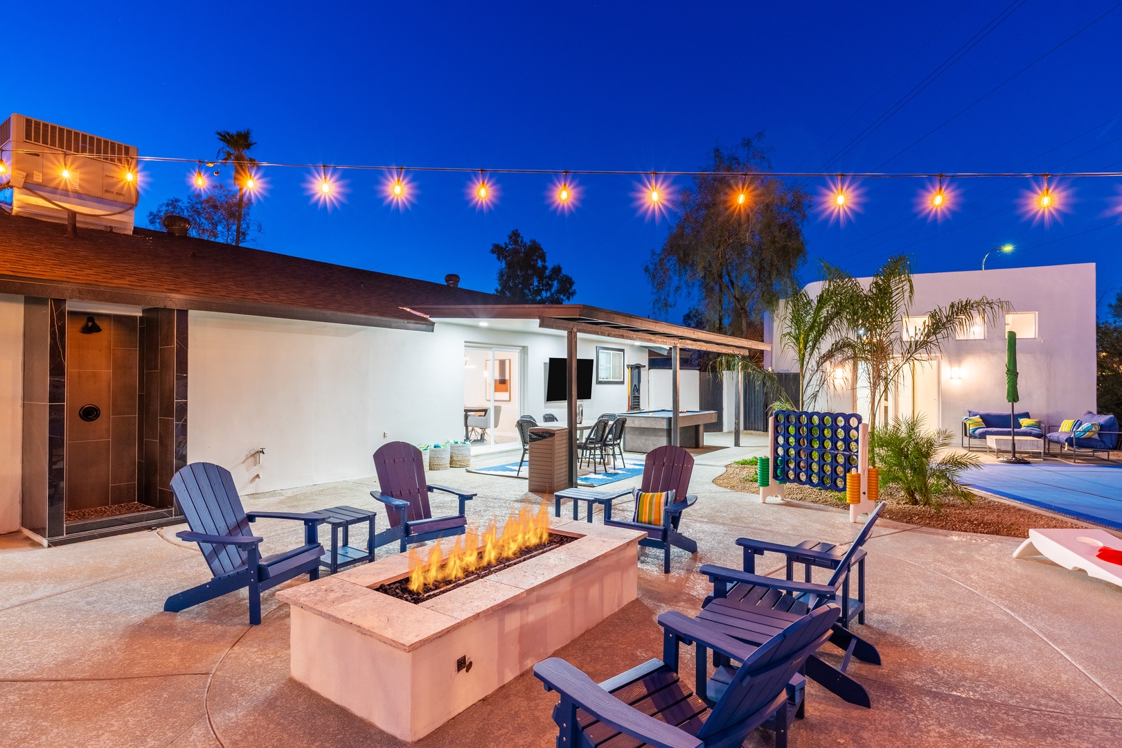The property's outdoor space features festive string lights, a modern fire pit with comfortable seating, and a spacious entertainment area perfect for relaxing evenings under the stars.