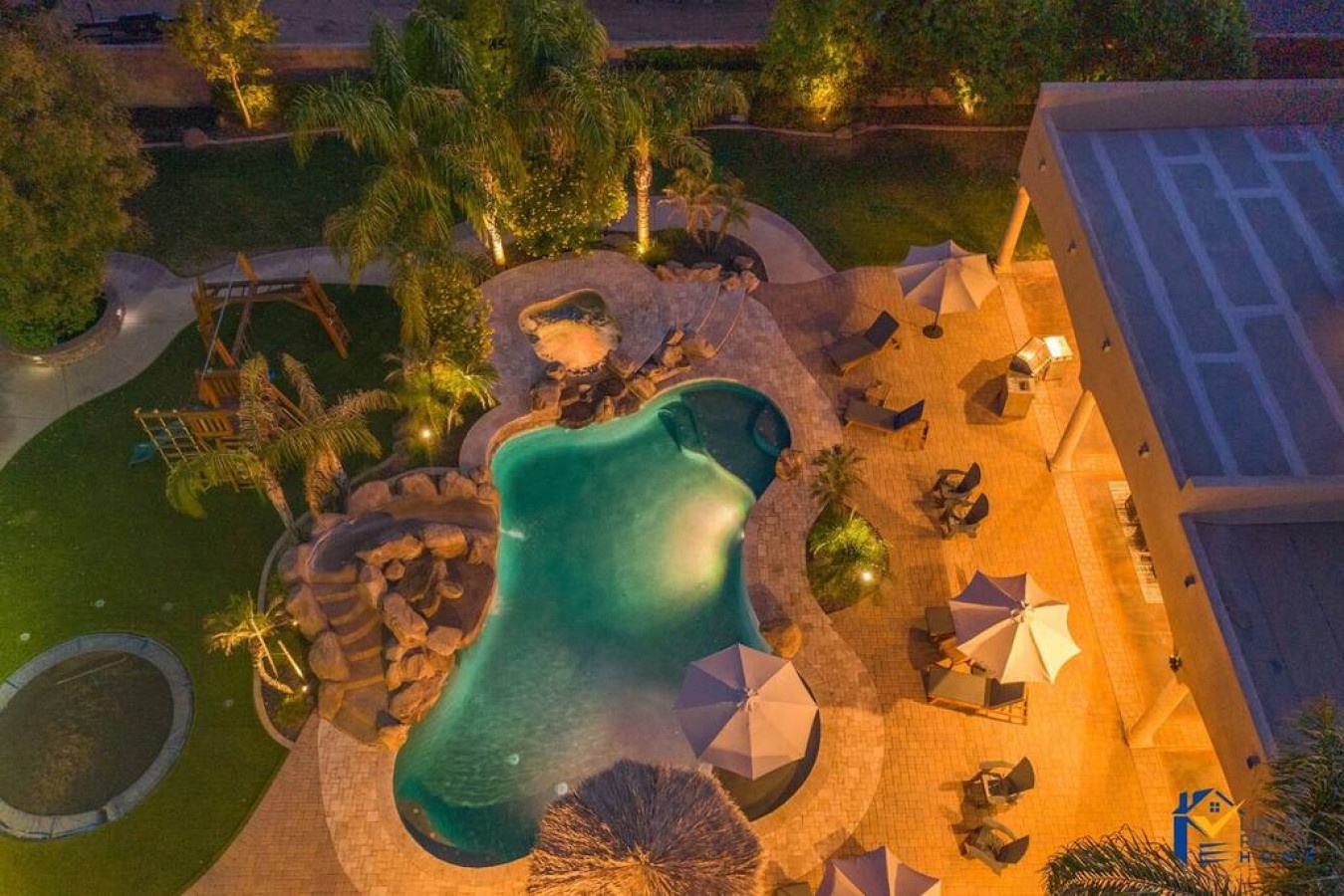 Stunning aerial view of the resort-style pool area with waterfall features and tropical landscaping creating an idyllic evening atmosphere.