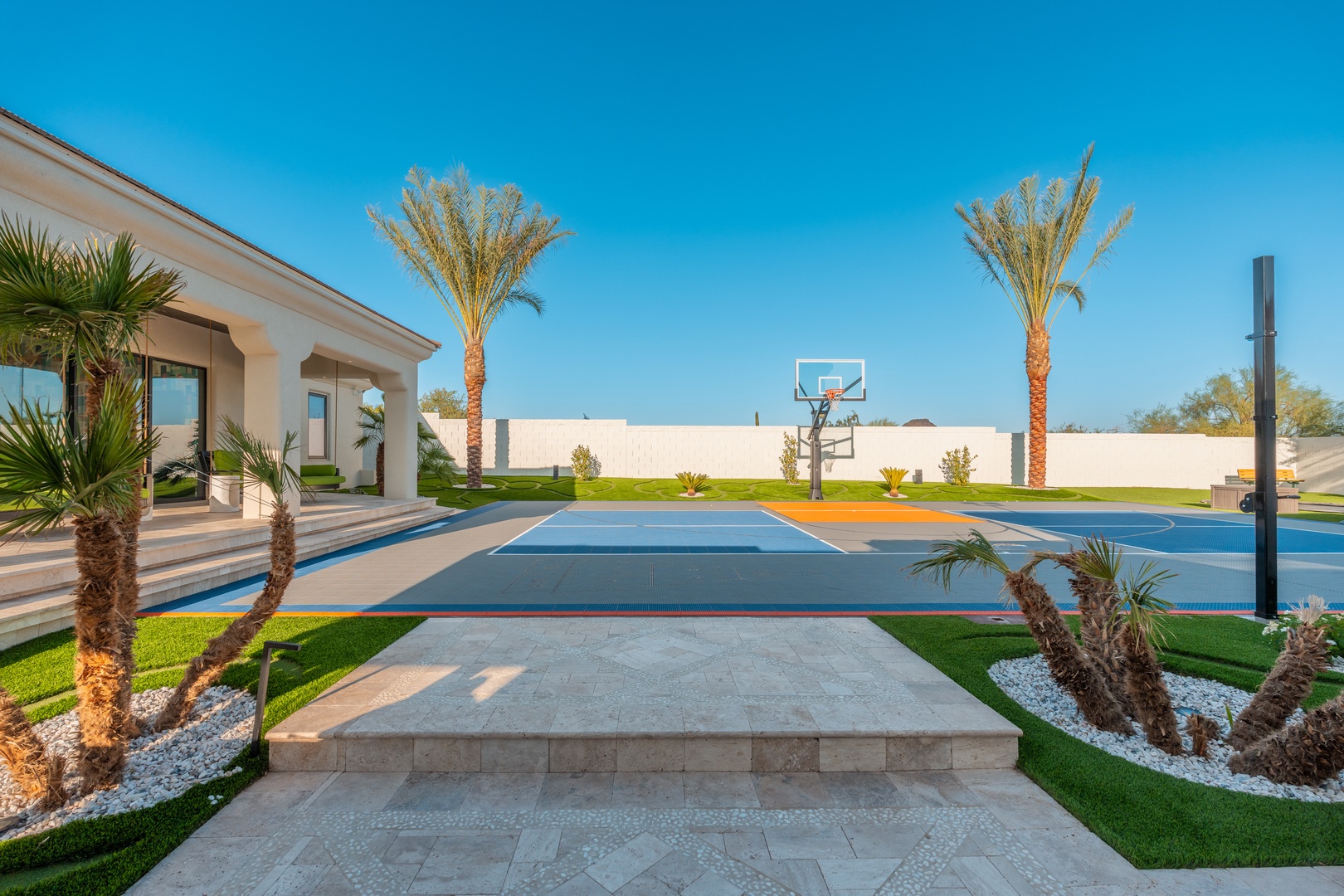 A private sport court framed by palm trees and manicured lawns, offering a sunny outdoor space for active days under clear blue skies.
