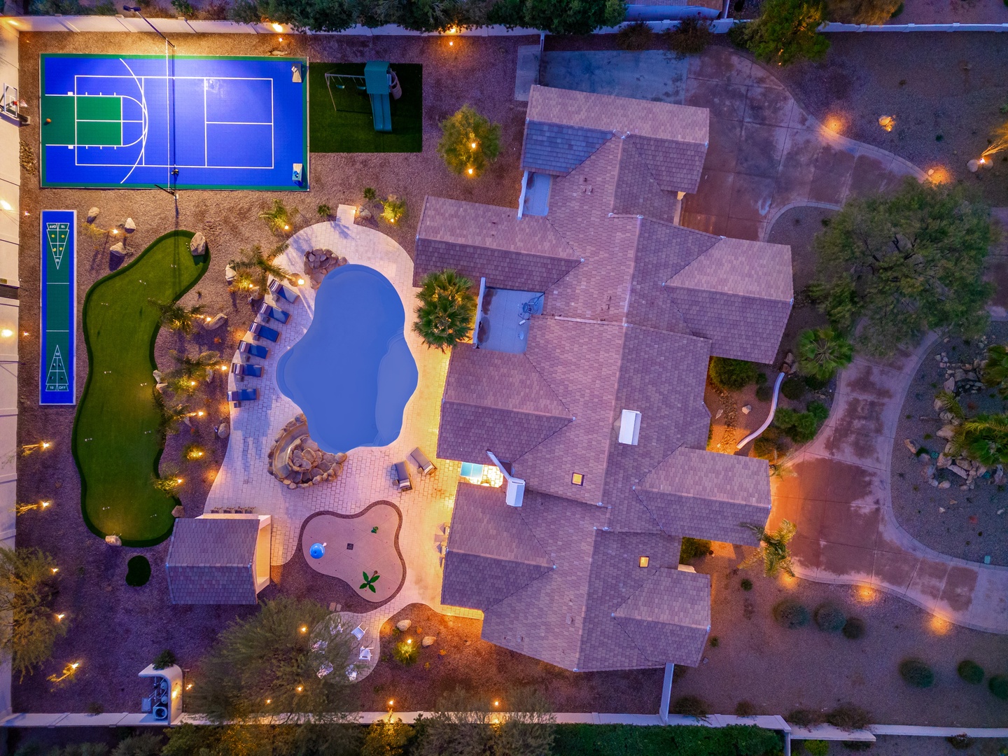 Aerial view showcasing the property's extensive recreational amenities, including a multi-court sports area, swimming pool, children's play zone, putting green, and beautifully lit grounds surrounding the villa—all part of the surrounding resort complex.