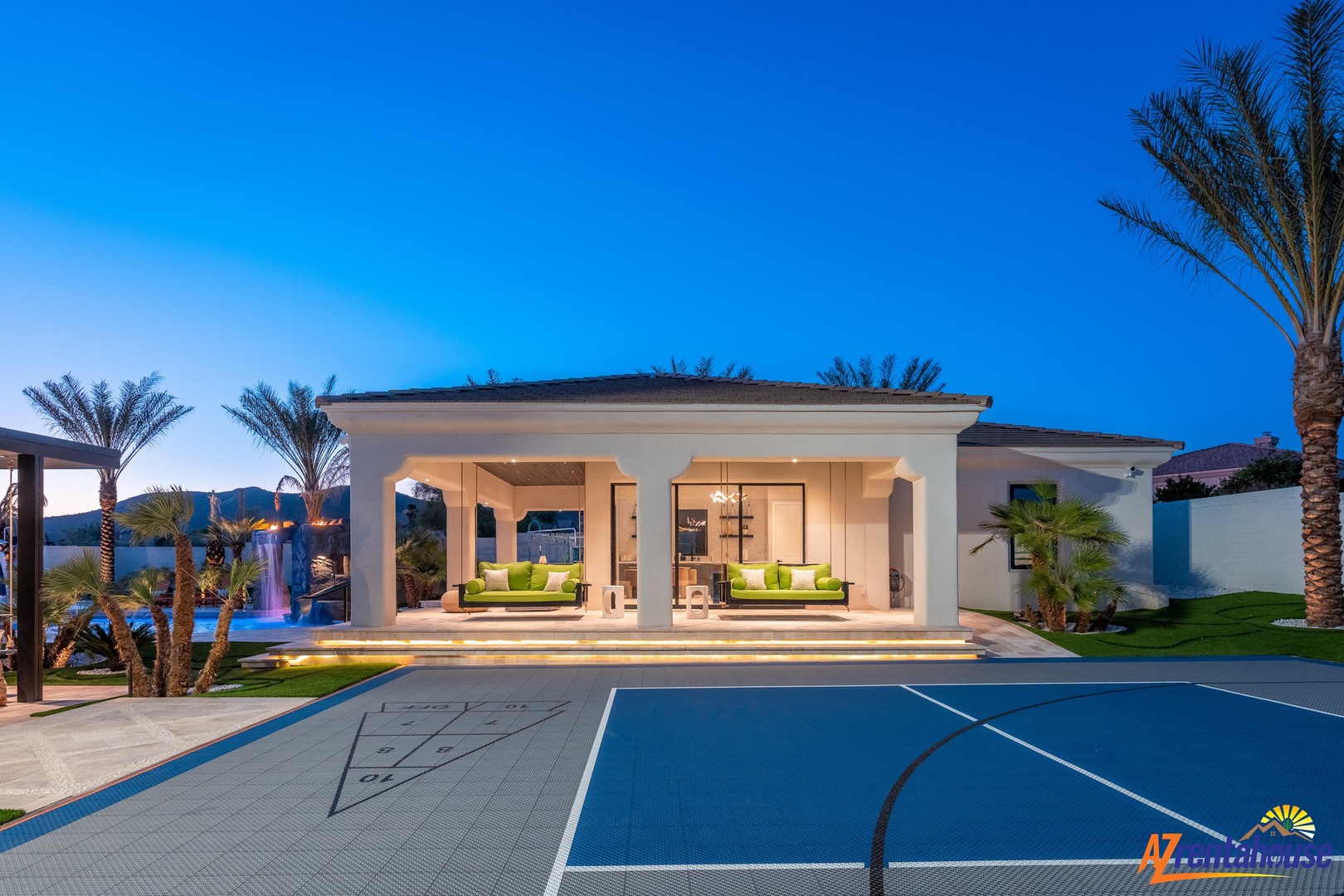 Modern luxury villa with elegant outdoor living spaces, surrounded by palm trees and mountain views at twilight.