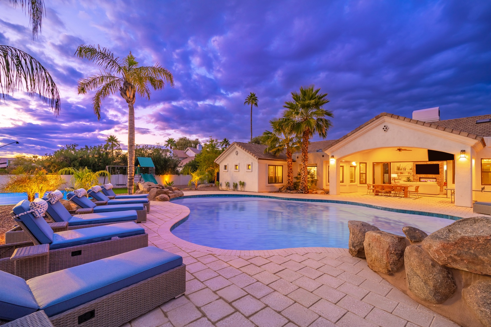 Stunning desert retreat featuring a pristine pool surrounded by swaying palms and luxury loungers, all bathed in twilight hues. The property's elegant architecture frames perfect evenings under painted skies.