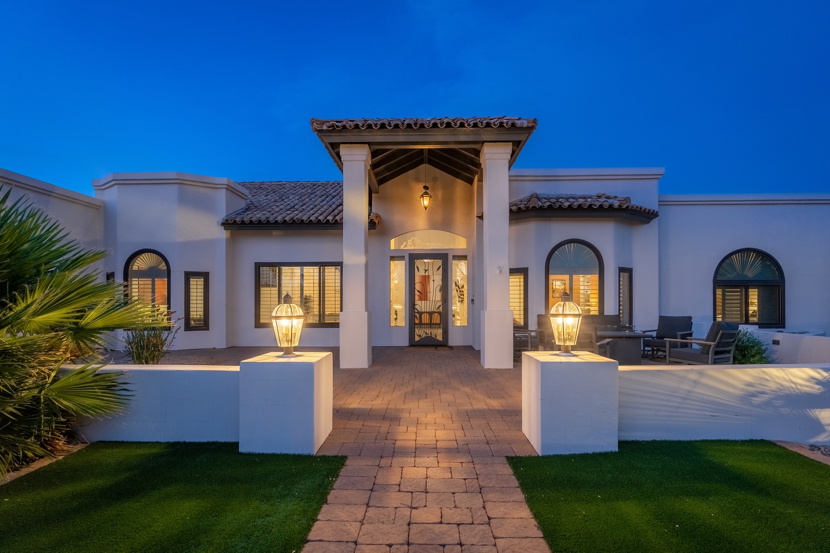 This elegant Spanish Colonial-style property welcomes guests with illuminated archways, stucco walls, and tiled roofing against a twilight sky—a serene arrival experience.