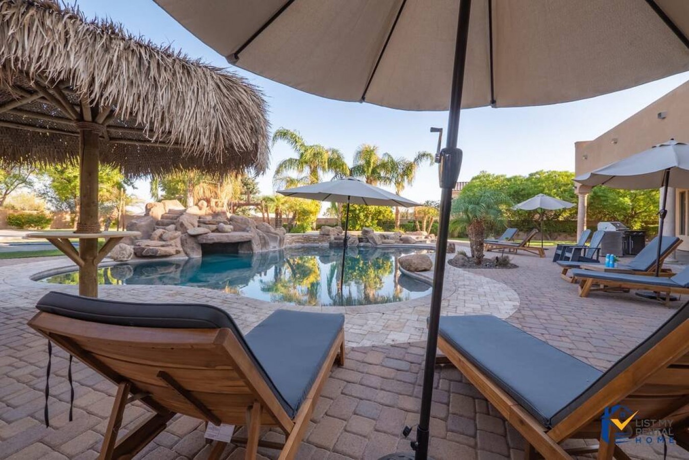 Unwind poolside on comfortable loungers beneath swaying palms and umbrellas, with tropical-inspired rock features creating your private resort-style oasis.