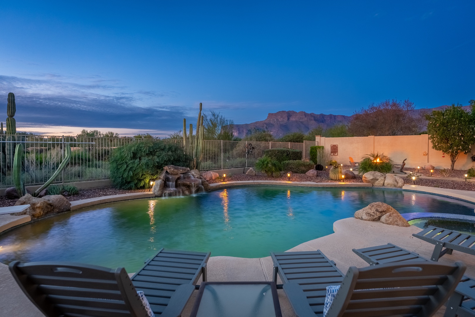 Stunning resort-style pool with natural rock waterfall and desert mountain views, perfect for twilight swims and starlit relaxation.