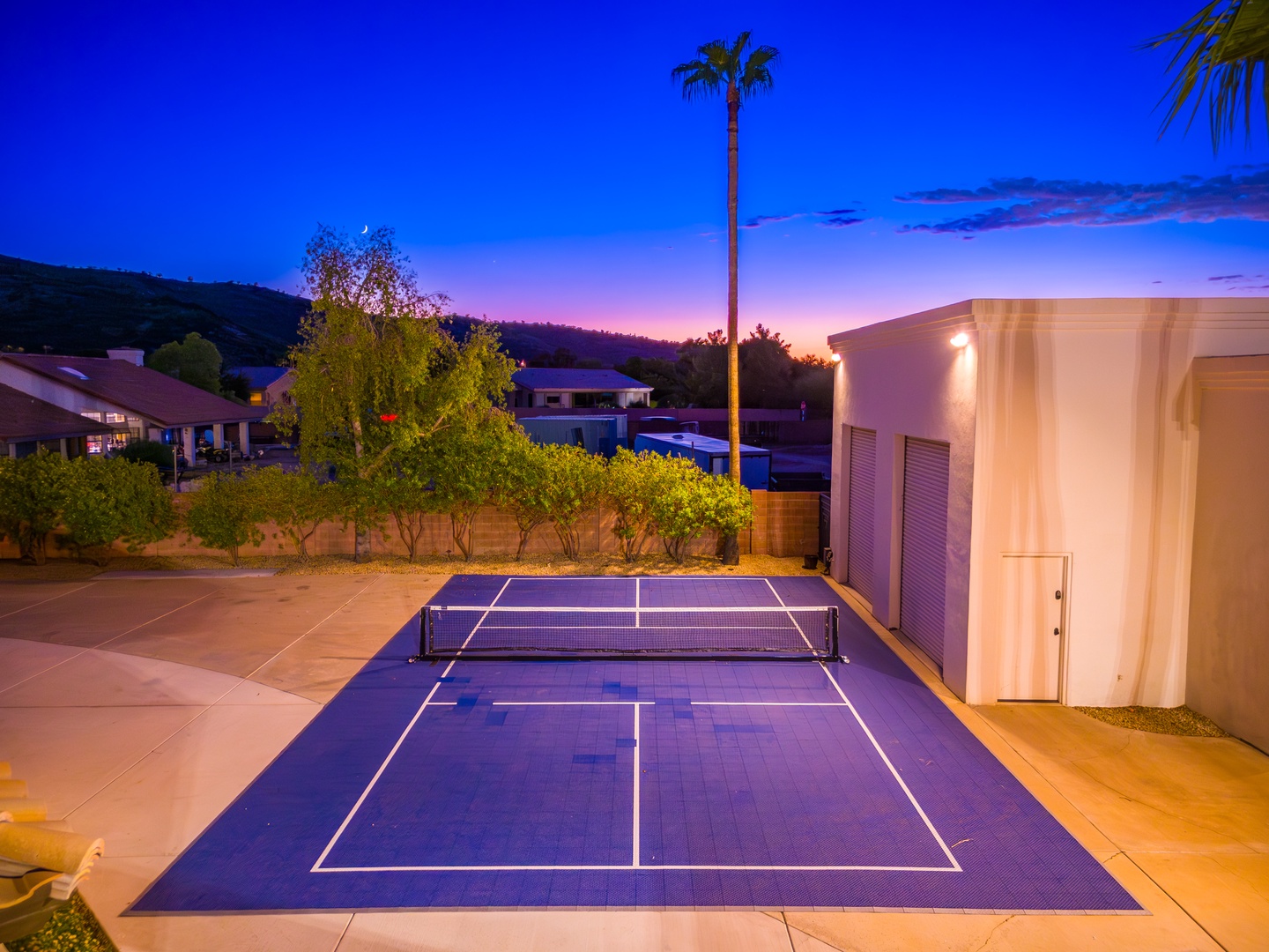 Your private pickleball court awaits under stunning twilight skies, framed by palm trees and hillside views—perfect for friendly matches and unforgettable evenings outdoors.