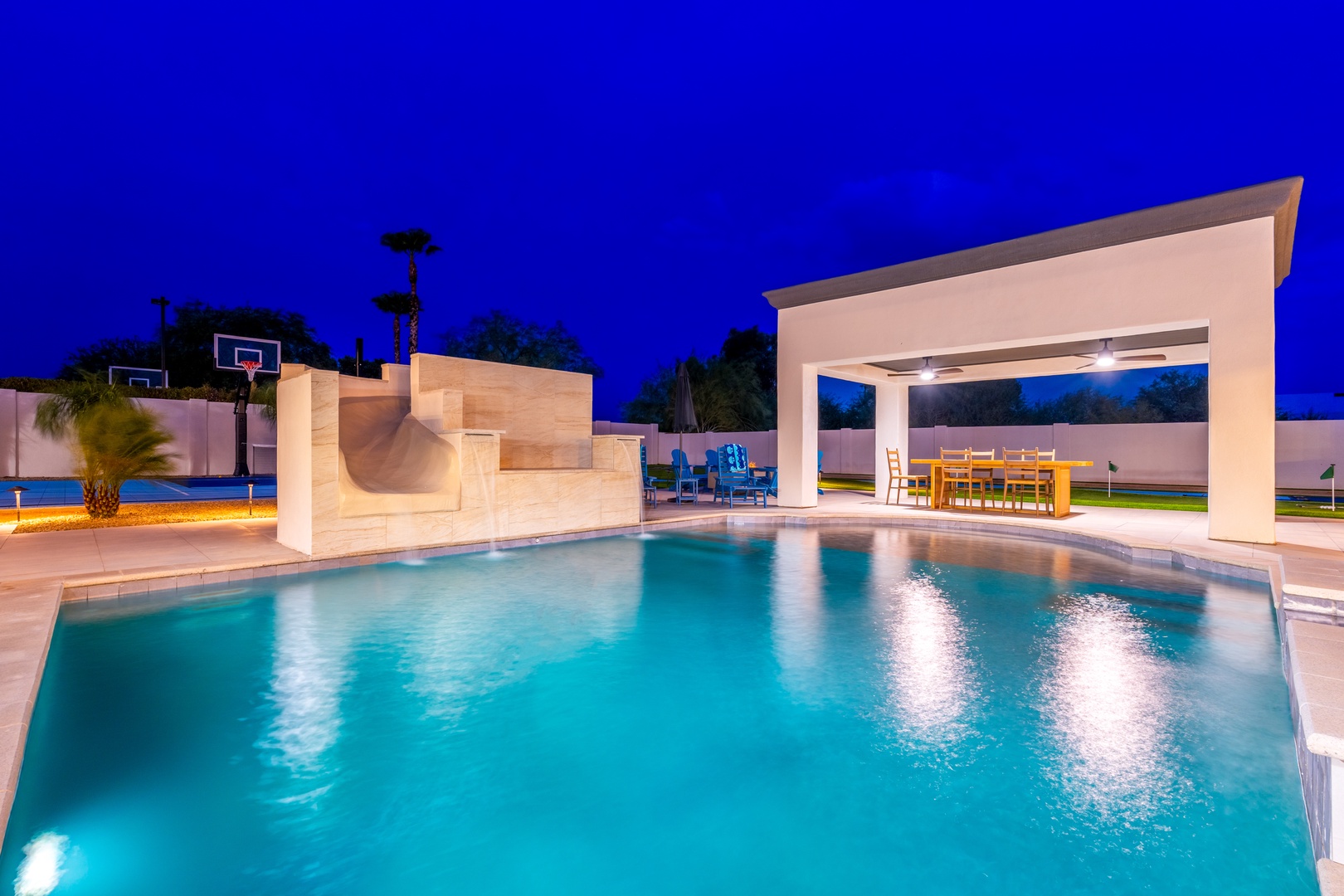 A stunning twilight view of the backyard features a pristine pool, covered dining pavilion, and sports court—ideal for evening gatherings and year-round fun.