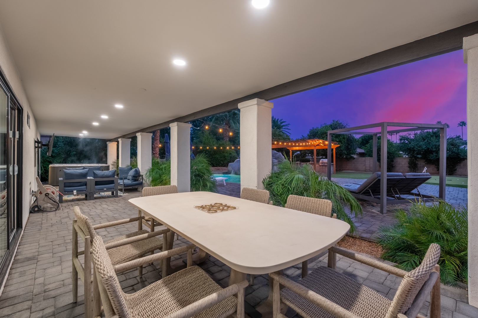Step outside to your covered patio where evening gatherings come alive under ambient string lights, with a sparkling pool and lush landscaping creating your private desert oasis.