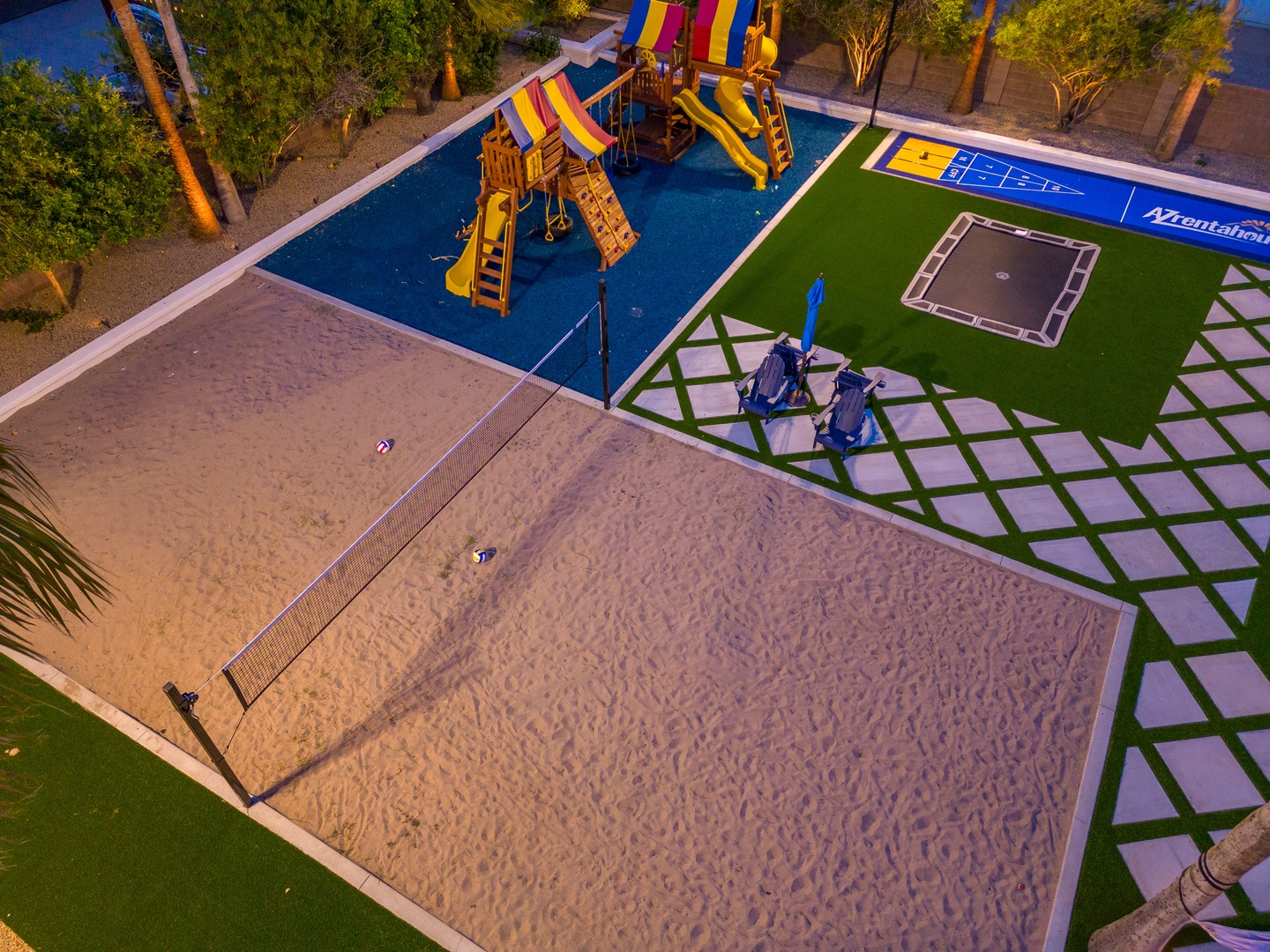 Aerial view of the property's recreational area featuring a colorful playground with slides, sand volleyball court, sports courts, and lush palm trees—ideal for active family fun.