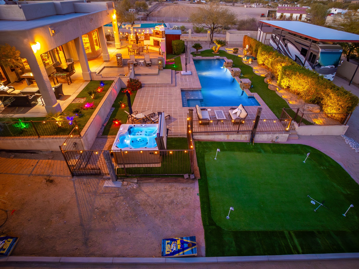 An aerial view showcases the property's expansive outdoor entertainment area, featuring a luxurious pool with waterfall feature, relaxing hot tub, putting green, multiple patio spaces, and lush landscaping illuminated for evening enjoyment.