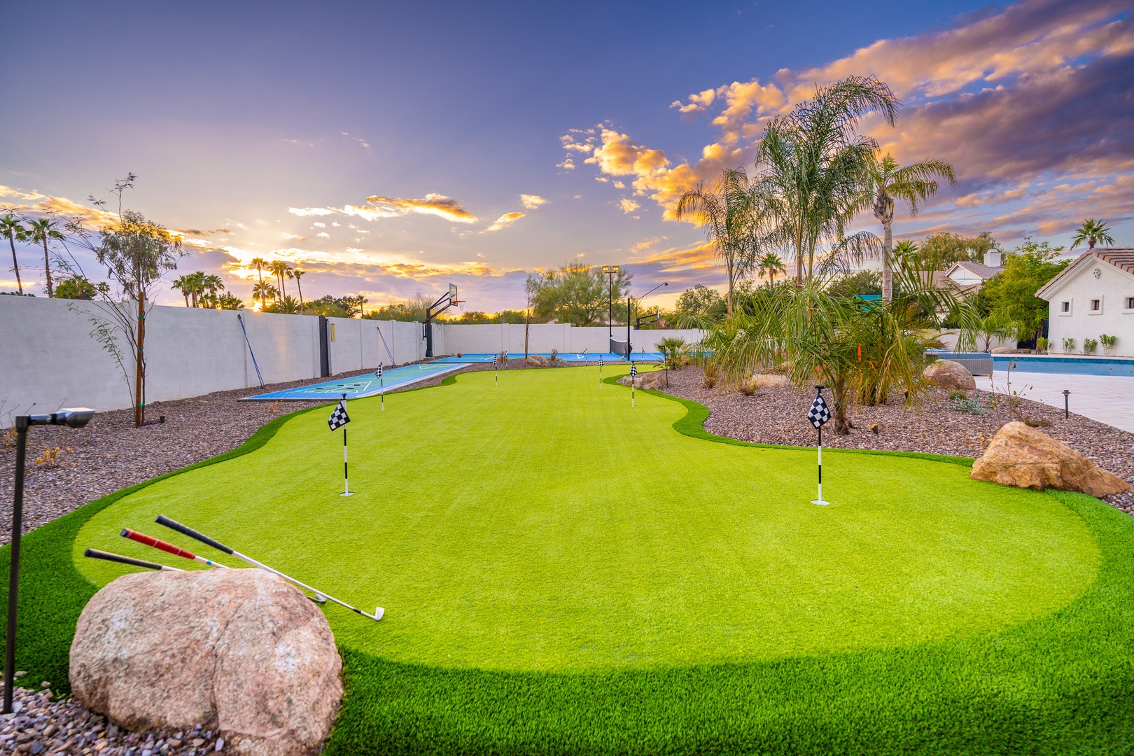 This desert oasis property features a private putting green, sparkling pool, and landscaped tropical yard with palm trees under vibrant Arizona skies at sunset.