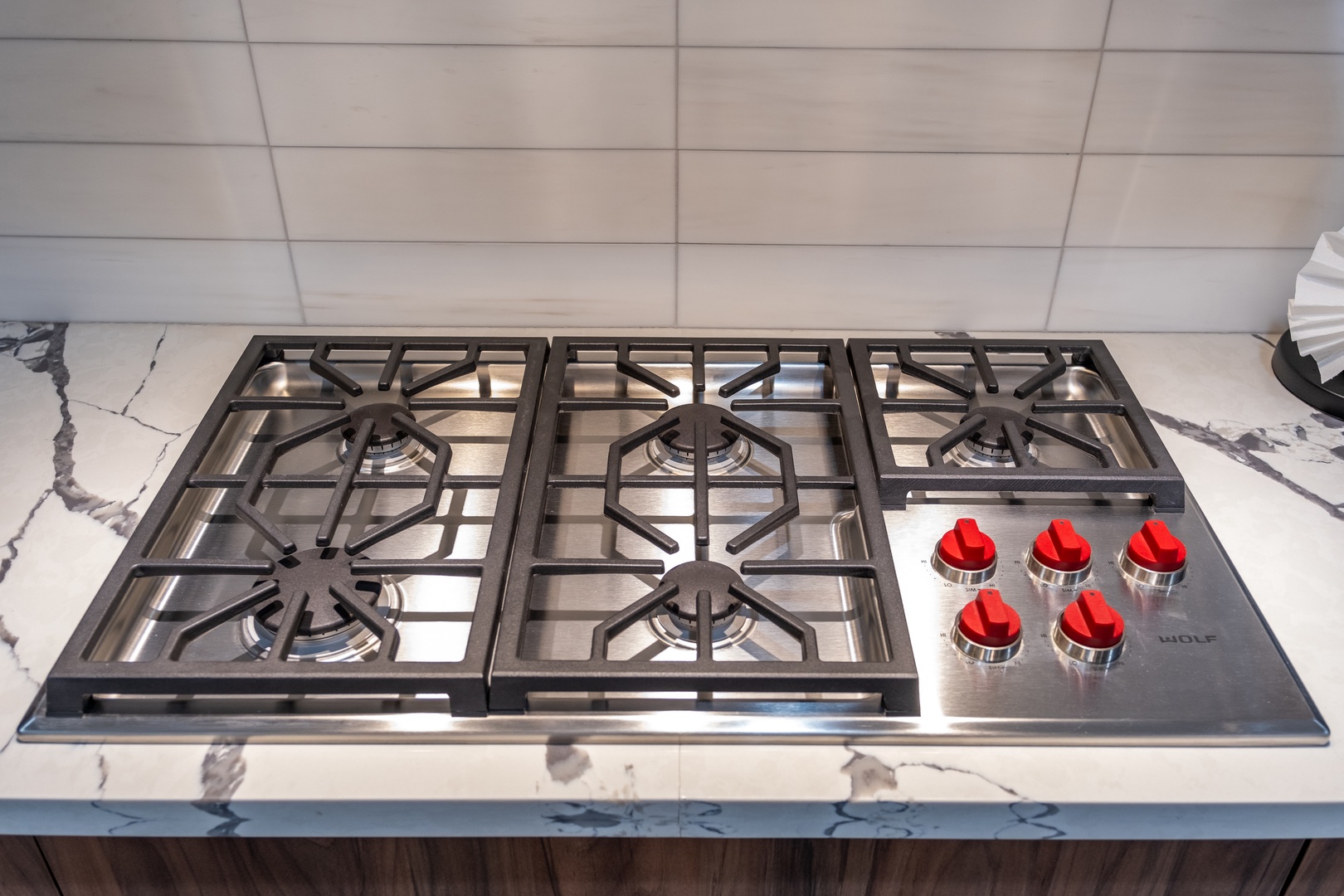 A sleek Wolf gas range with bright red knobs sits ready on stunning marble countertops, inviting you to create culinary masterpieces during your stay.