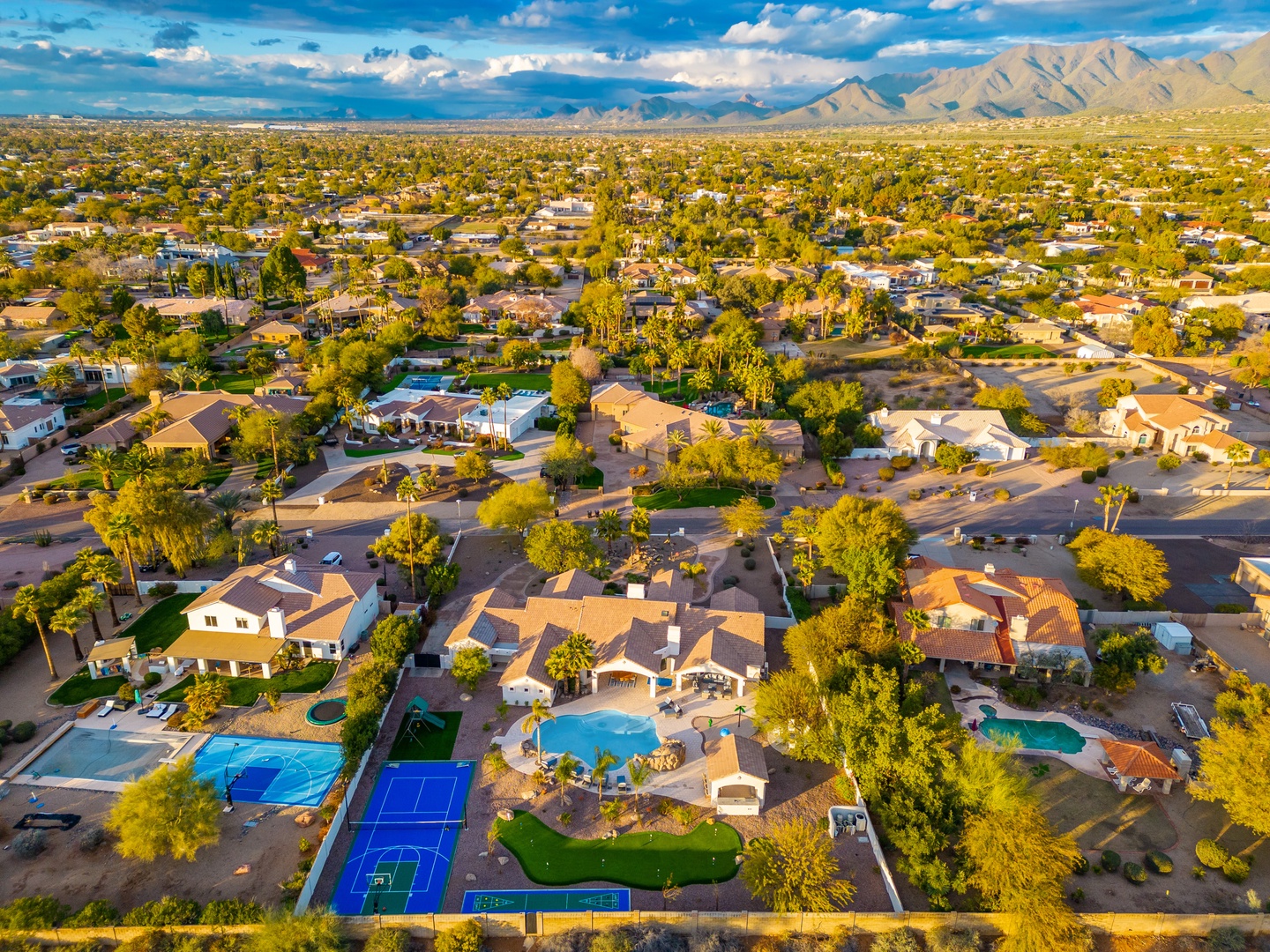 Aerial view of a desert neighborhood featuring pools, sports courts, and mountain vistas—part of the property's surrounding area.