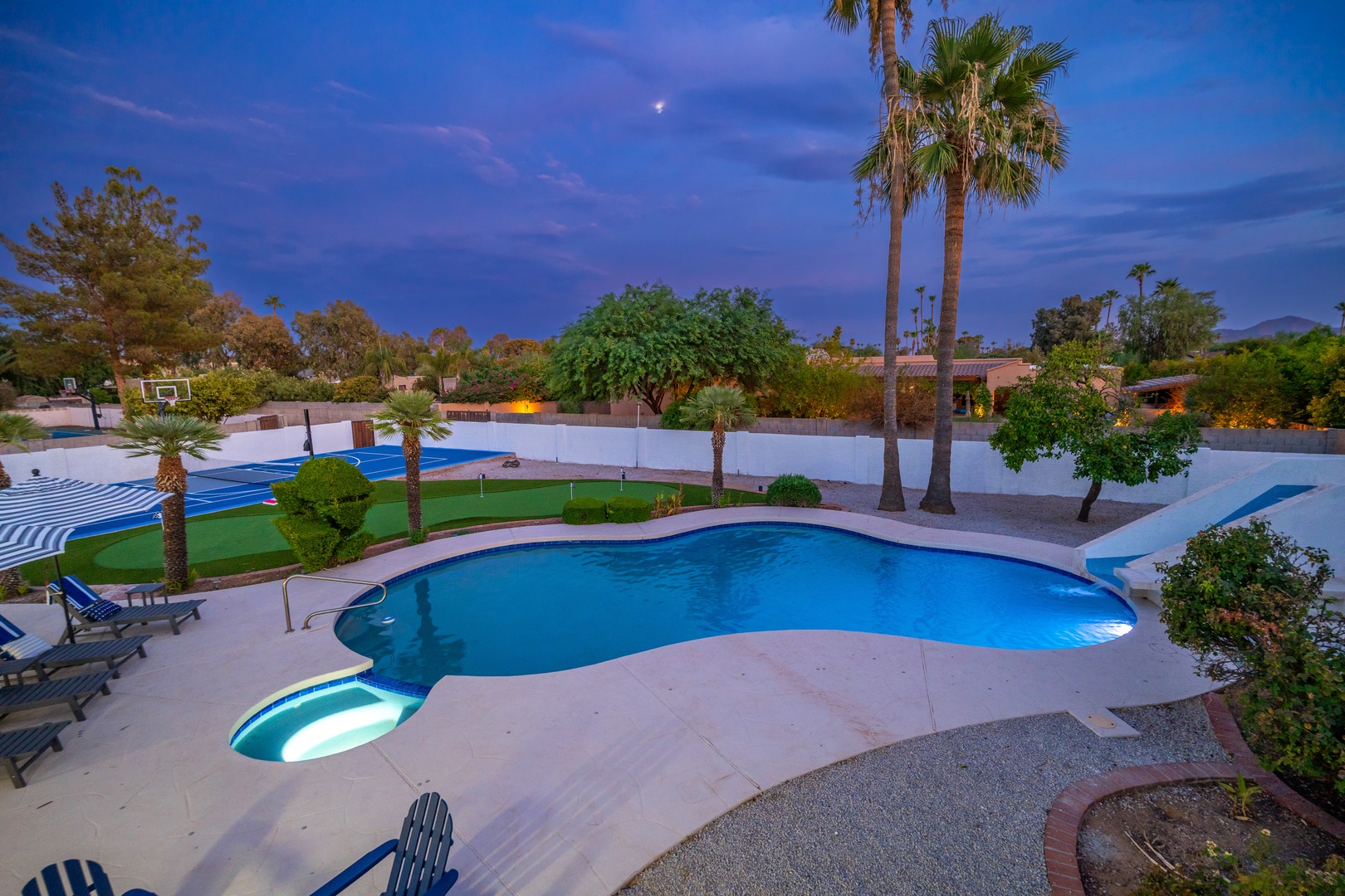 Private oasis at twilight features a freeform pool with spa, lush palm trees, and manicured lawn set against a stunning desert sky backdrop.