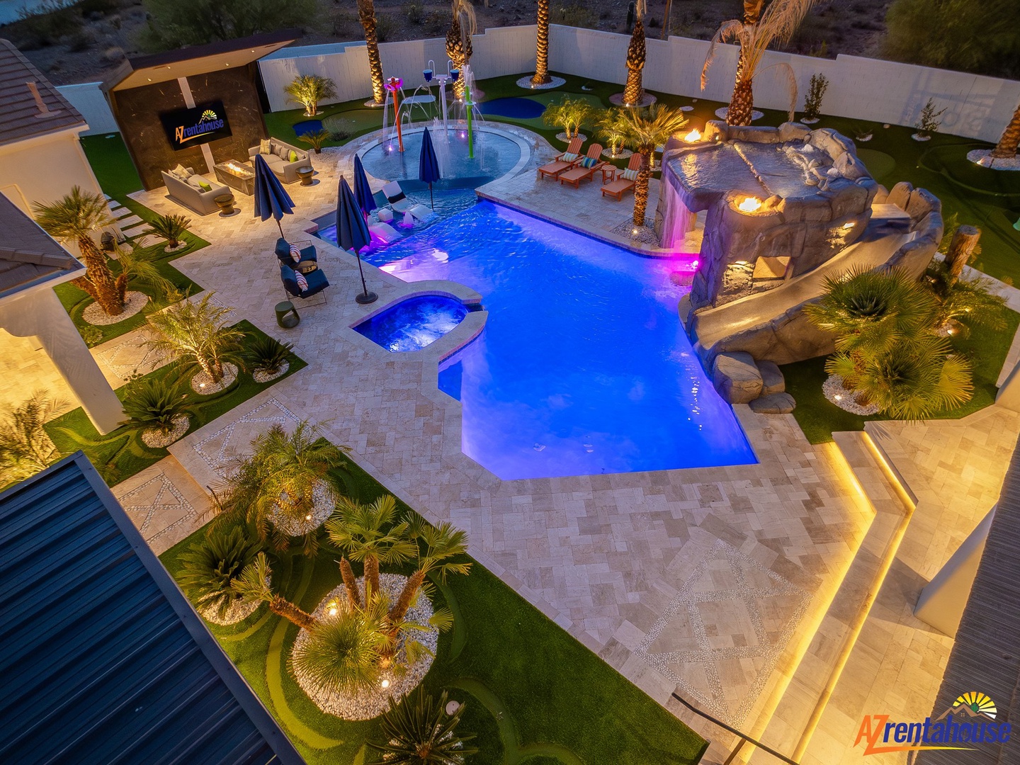 Stunning aerial view of a luxurious desert oasis with resort-style pool, hot tub, and palm trees illuminated at dusk.