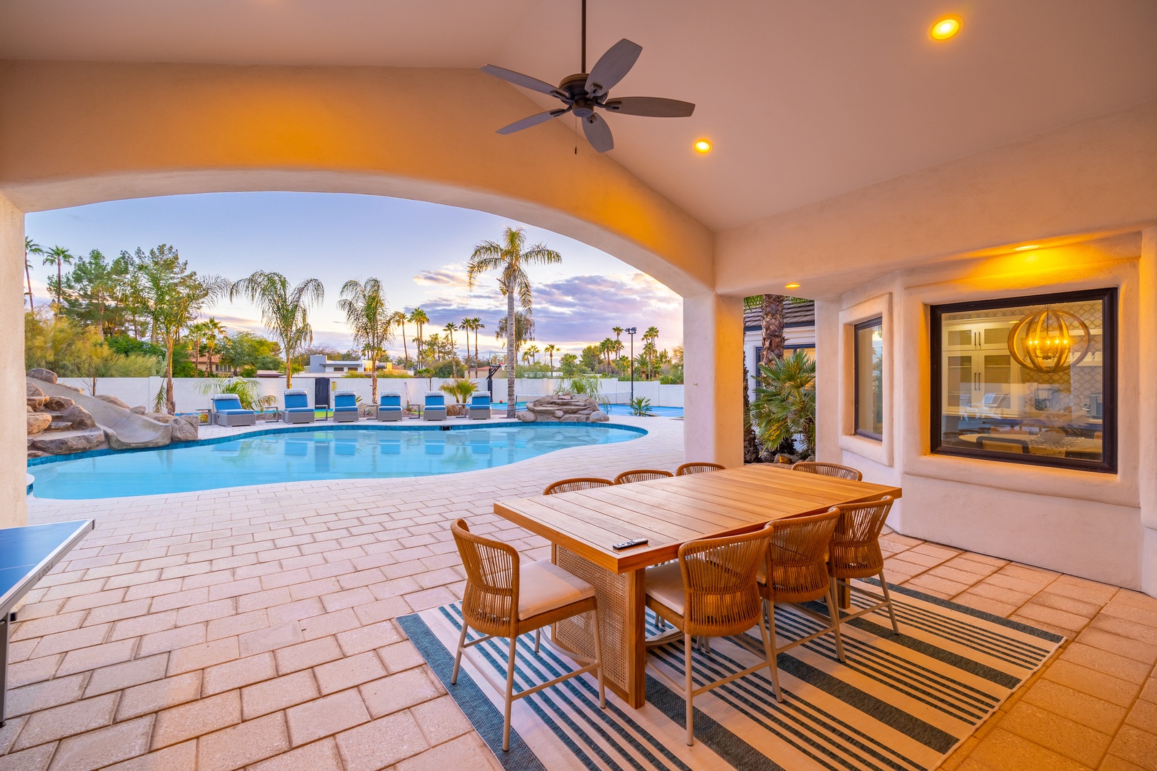 Enjoy al fresco dining under a graceful archway that frames stunning desert and pool views, perfect for memorable meals beneath swaying palms and golden skies.