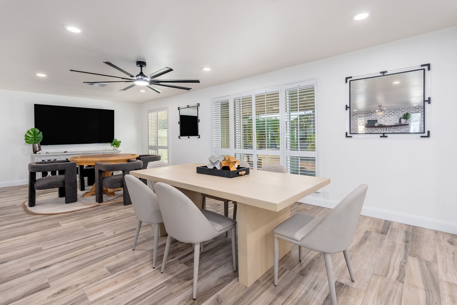 Your spacious dining and entertainment area features modern furnishings, a large flat-screen TV, and natural light streaming through plantation shutters—perfect for gathering with family and friends.
