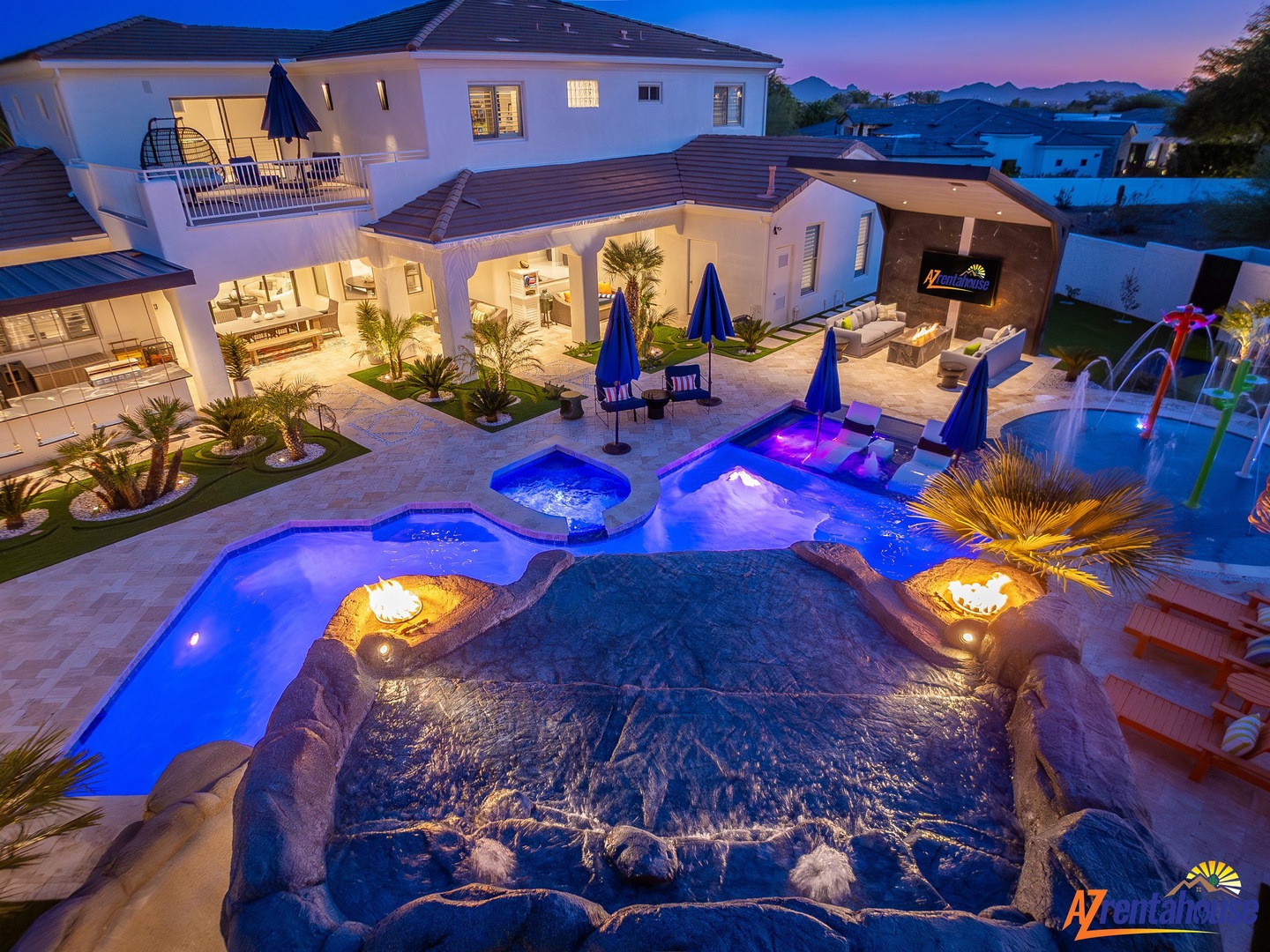 Stunning villa showcases illuminated pools, hot tub, and elegant outdoor living spaces at twilight.