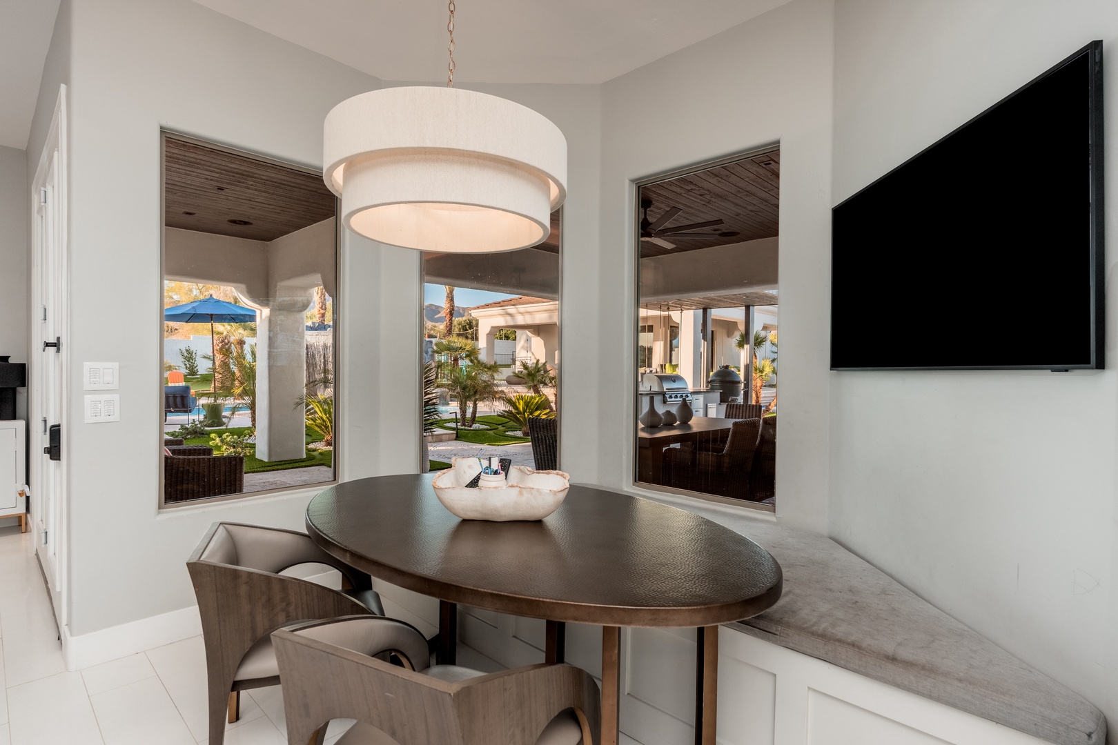 Your bright dining nook flows seamlessly into the lush garden through expansive windows, blending indoor comfort with outdoor serenity. Enjoy meals under elegant lighting while admiring mountain views and palm trees.