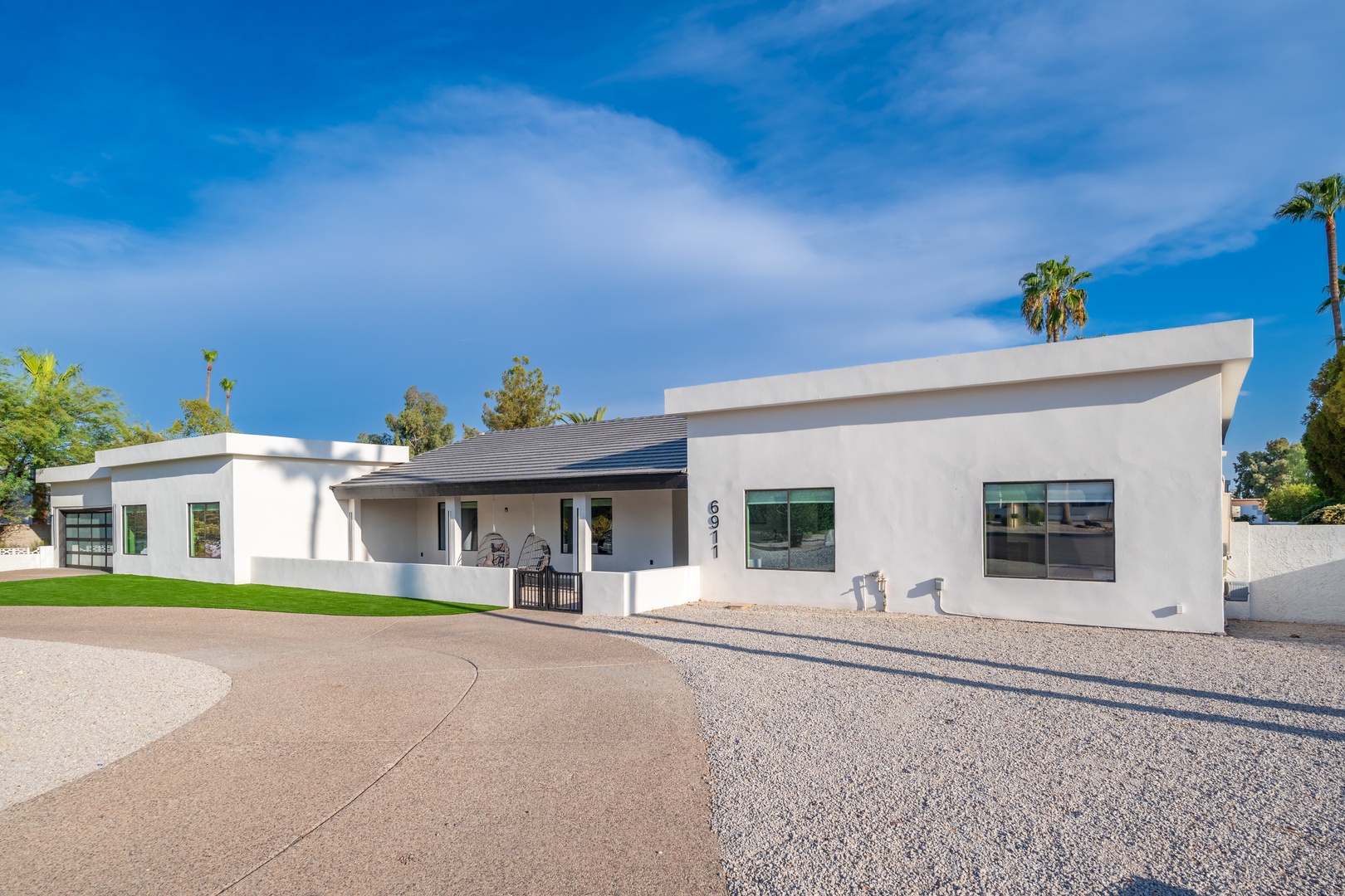 Modern single-story vacation home featuring clean architectural lines, surrounded by desert landscaping and palm trees under bright Arizona skies.
