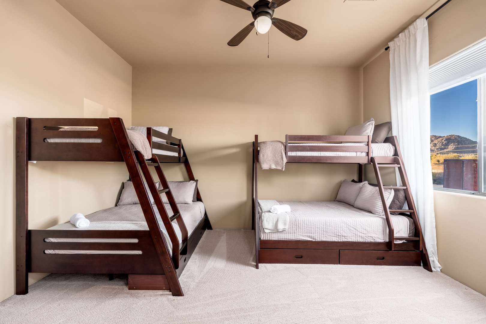 Two sturdy bunk beds dressed in crisp white linens create a cozy sleeping haven for the whole family. A ceiling fan keeps the air fresh, while the window frames stunning mountain views perfect for daydreaming.