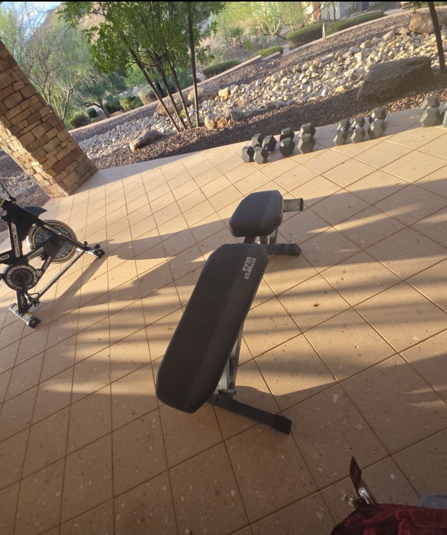 A private patio fitness area awaits, complete with a weight bench and exercise bike, overlooking a peaceful landscaped courtyard—perfect for your morning workout routine.