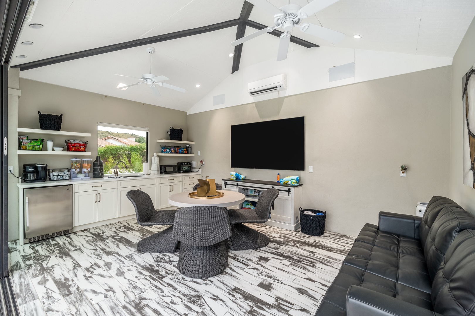 Unwind in your private entertaining space with a kitchenette, flat-screen TV, comfortable seating, and high ceilings with natural light streaming through the window.
