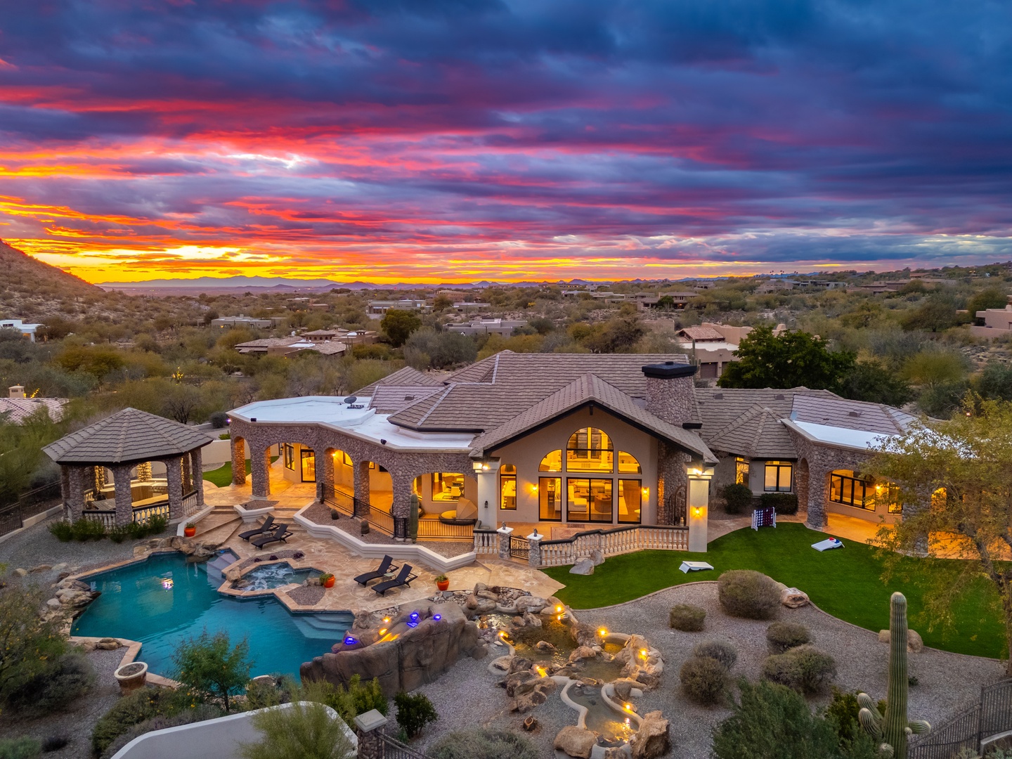 A luxurious desert estate framed by a vibrant sunset, featuring an expansive pool, outdoor entertaining spaces, and stunning natural surroundings.