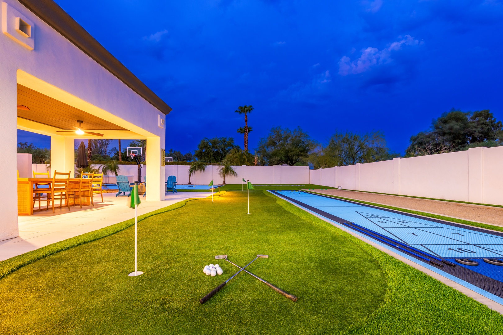 The property features a private backyard with a long lap pool, putting green, covered patio, and spacious lawn area surrounded by privacy fencing—captured during twilight hours.