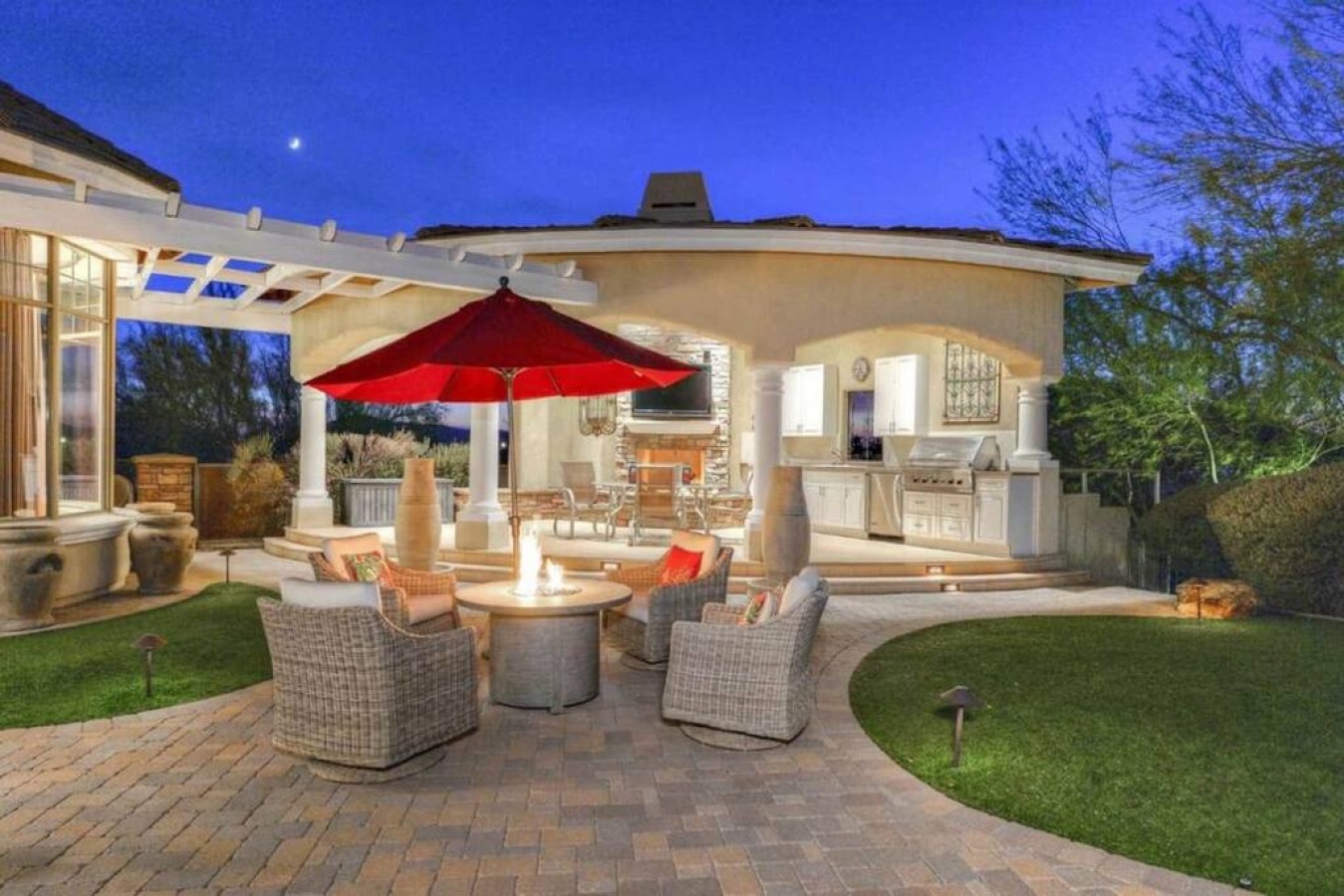Elegant outdoor living area with covered patio, built-in grill, and cozy fire pit seating, ideal for evening gatherings under a twilight sky.