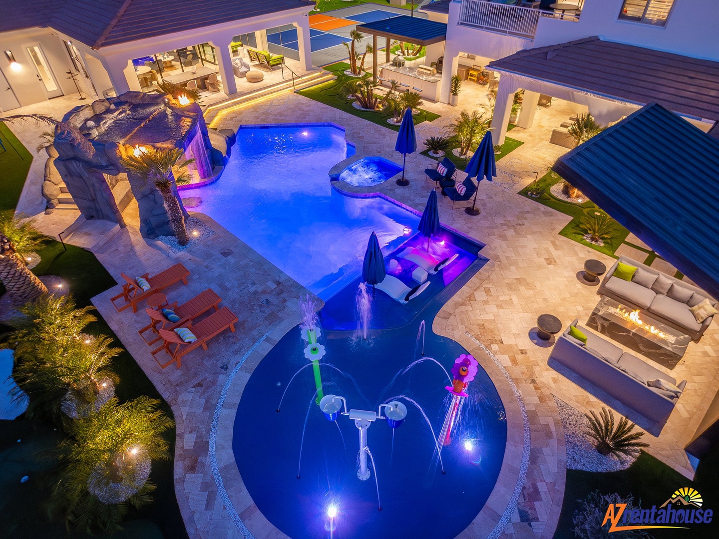 Stunning aerial view of a luxury pool complex with spa features, colorful lighting, and expansive outdoor entertaining areas.