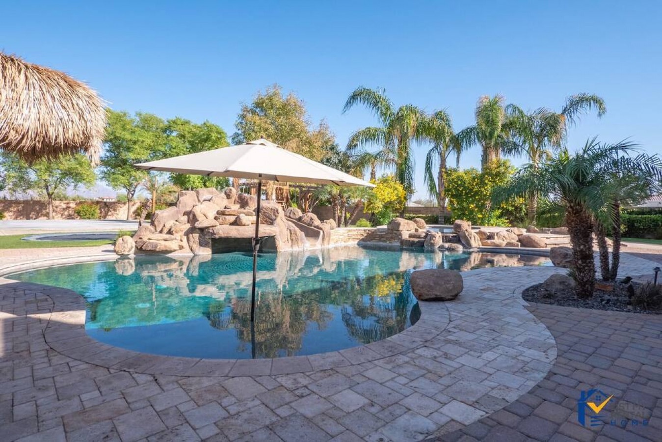 Dive into your private tropical oasis featuring a stunning rock waterfall pool surrounded by lush palms and desert landscaping.