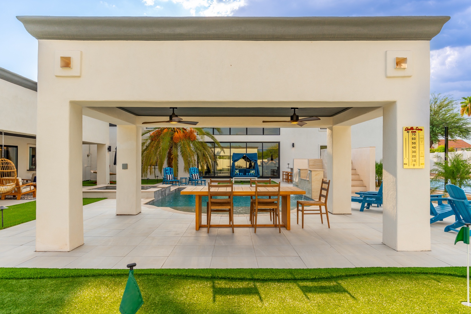 A modern covered pavilion frames a sparkling pool and outdoor dining area, perfect for warm-weather gatherings with palm trees swaying overhead.
