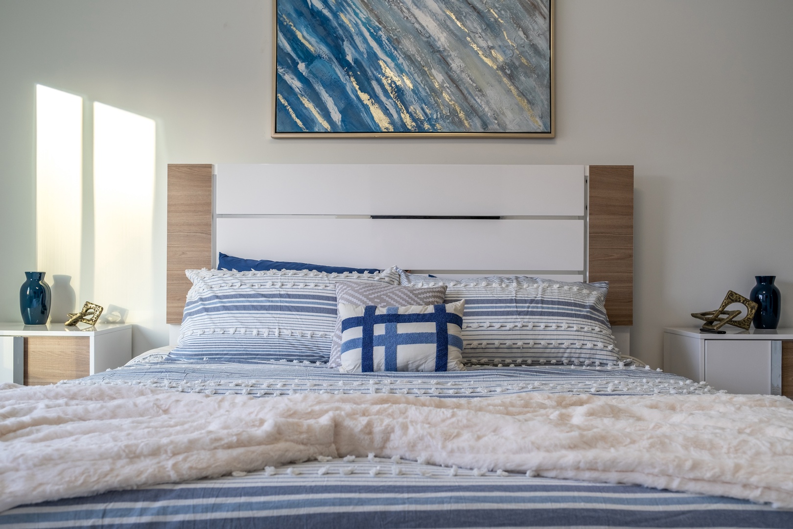 Sink into this plush bed adorned with calming blues and soft textures. Morning light and coastal-inspired decor create your serene escape for restful nights.