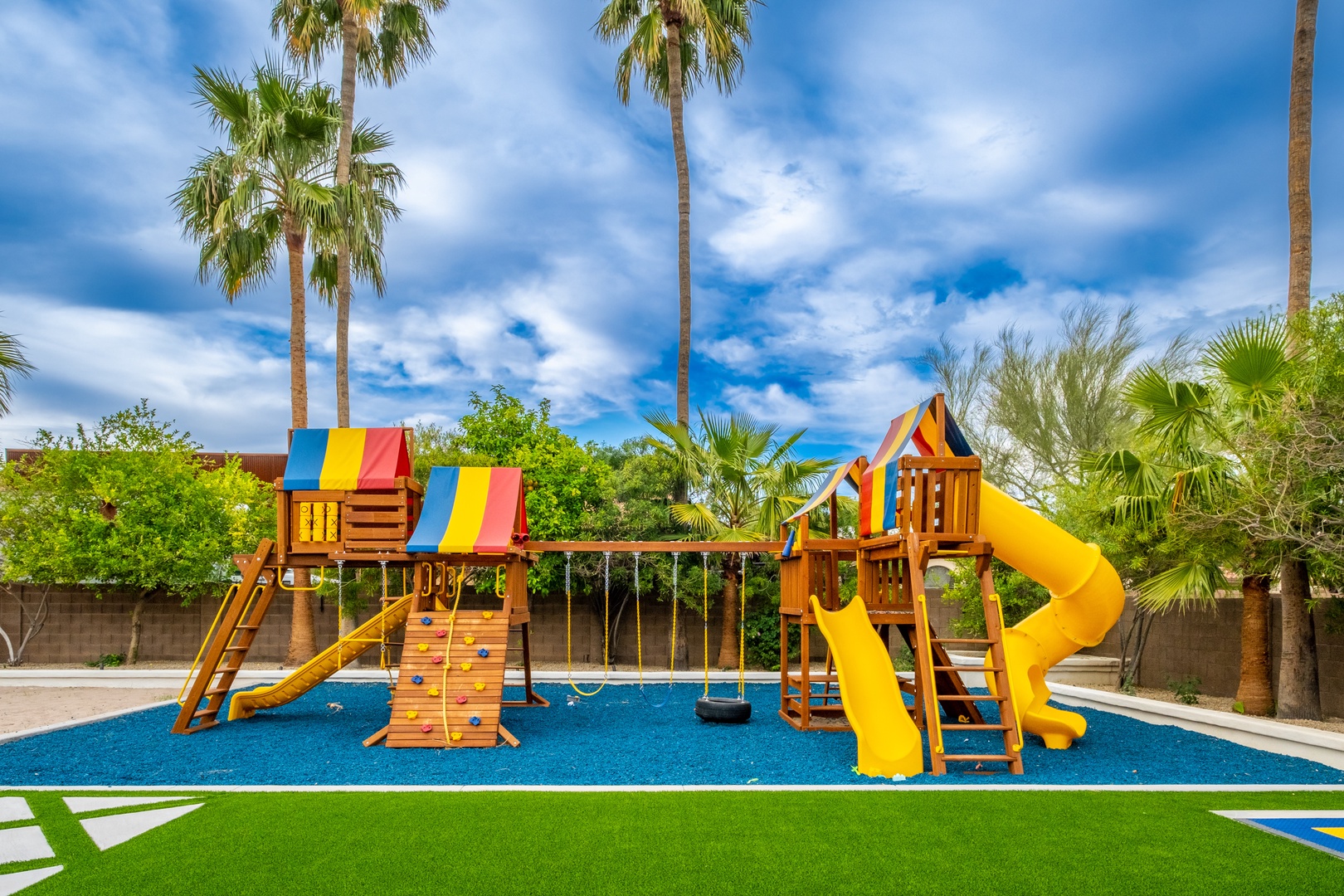 A vibrant playground awaits with climbing walls, swings, and bright yellow slides, all under swaying palms and sunny skies—perfect for hours of outdoor fun.