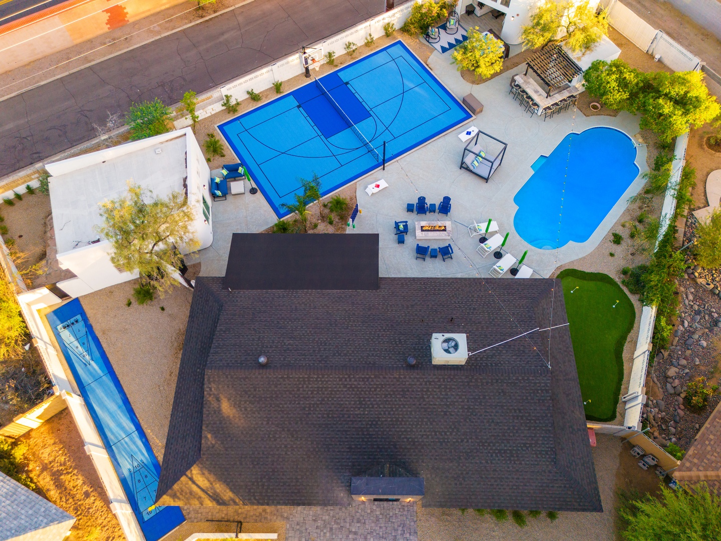 Aerial view showcasing the property's extensive recreation area featuring a full basketball court, freeform pool, putting green, and multiple outdoor dining and lounging spaces.