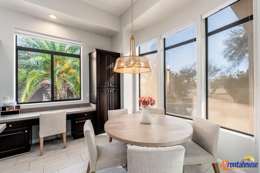 Your bright dining nook features a stylish round table and copper pendant light, surrounded by large windows showcasing tropical greenery.