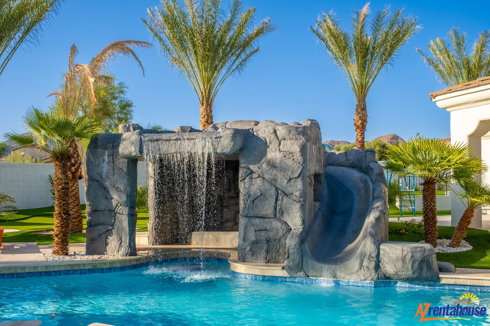 Dive into your private oasis with this stunning rock waterfall feature, surrounded by swaying palms under endless blue skies.