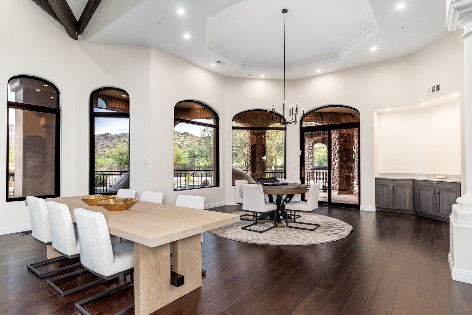 Picture yourself dining in this elegant space where natural light floods through arched windows and vaulted ceilings create an airy, sophisticated atmosphere. Your meals will feel special at the beautiful wood table, with desert views creating a serene ba