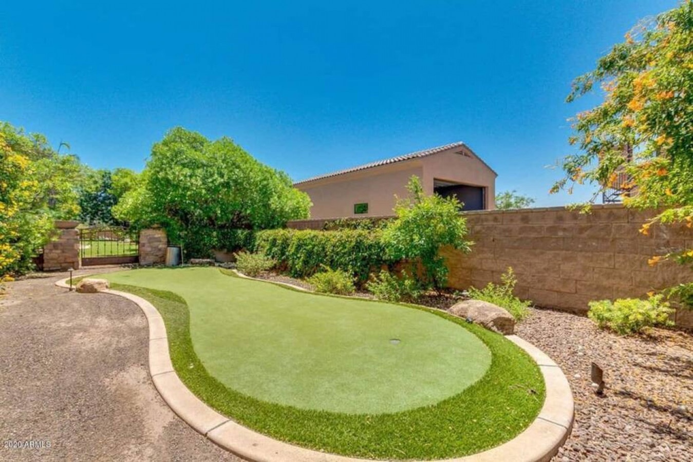 Modern desert home features private putting green surrounded by lush landscaping and mature trees under Arizona's endless blue skies.