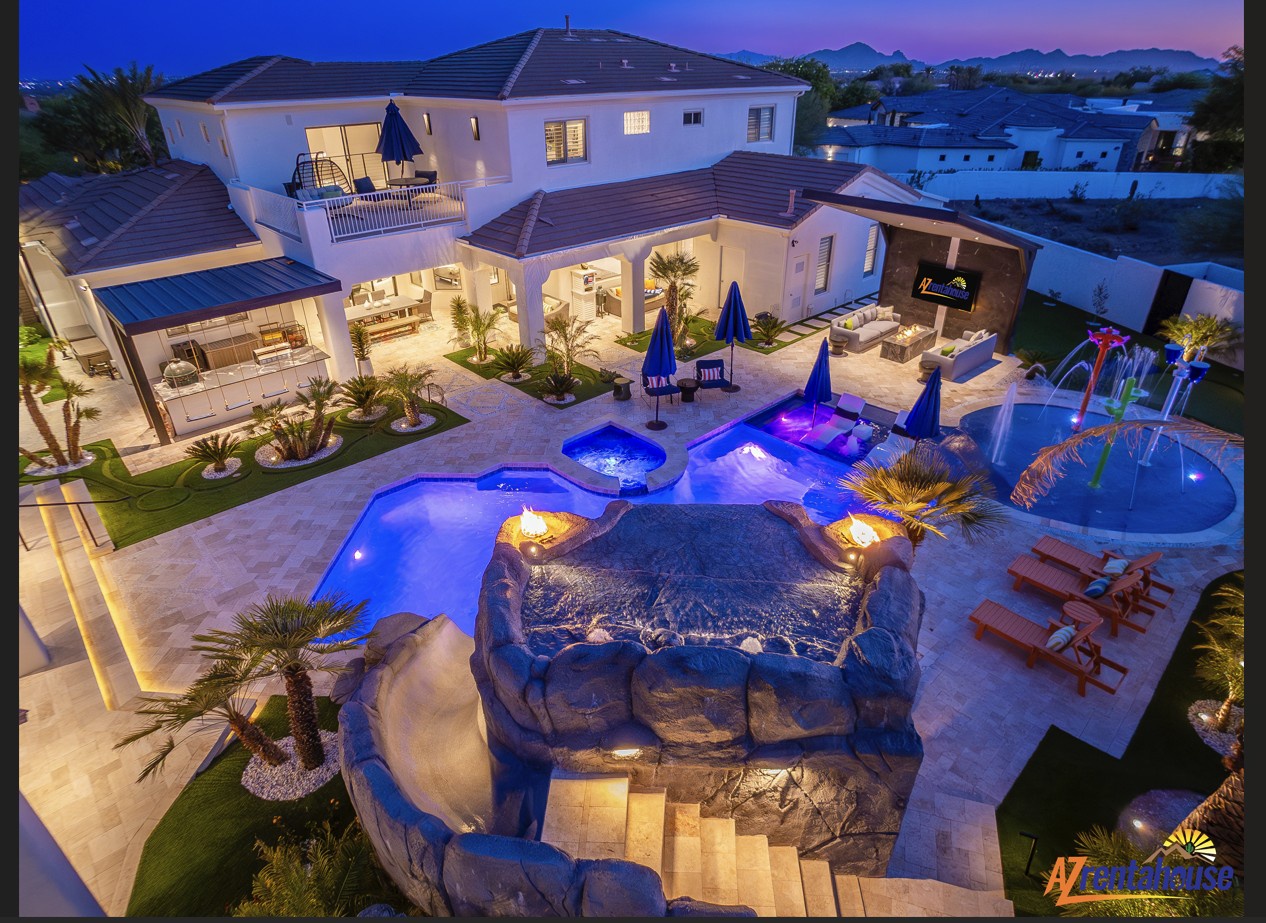 Stunning aerial view of luxury villa with custom rock waterfall pool and illuminated outdoor living spaces at twilight.