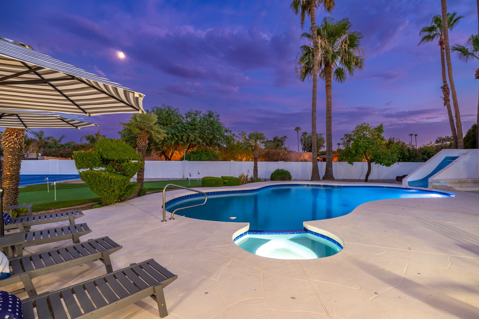 A stunning desert sunset paints the sky in purple and pink hues as palm trees sway over the sparkling pool and integrated spa—a perfect backdrop for tranquil evening swims and peaceful relaxation.