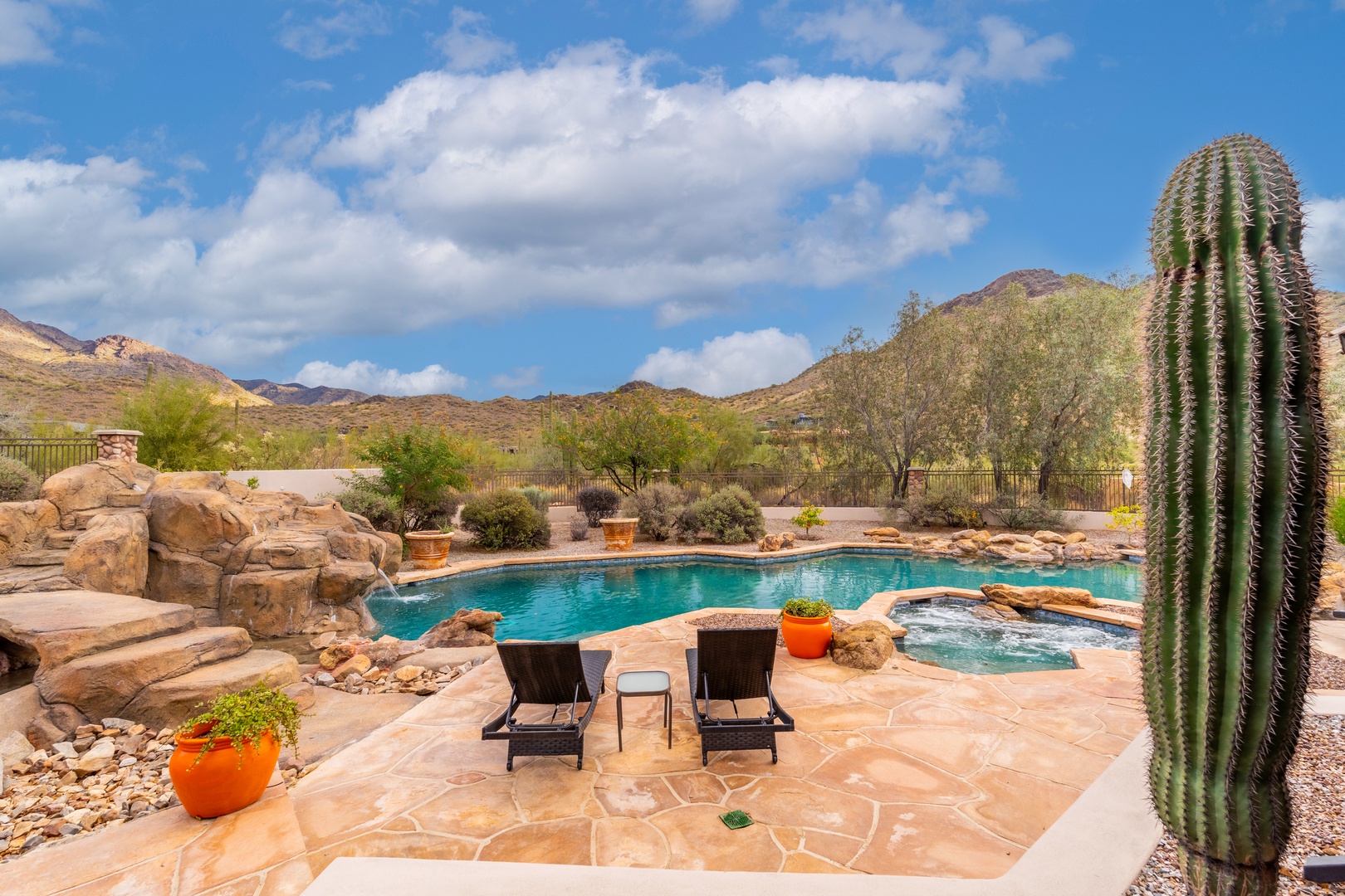 The resort-style pool area offers stunning mountain views and natural desert landscaping with towering cacti, stone accents, and a built-in spa for ultimate relaxation.