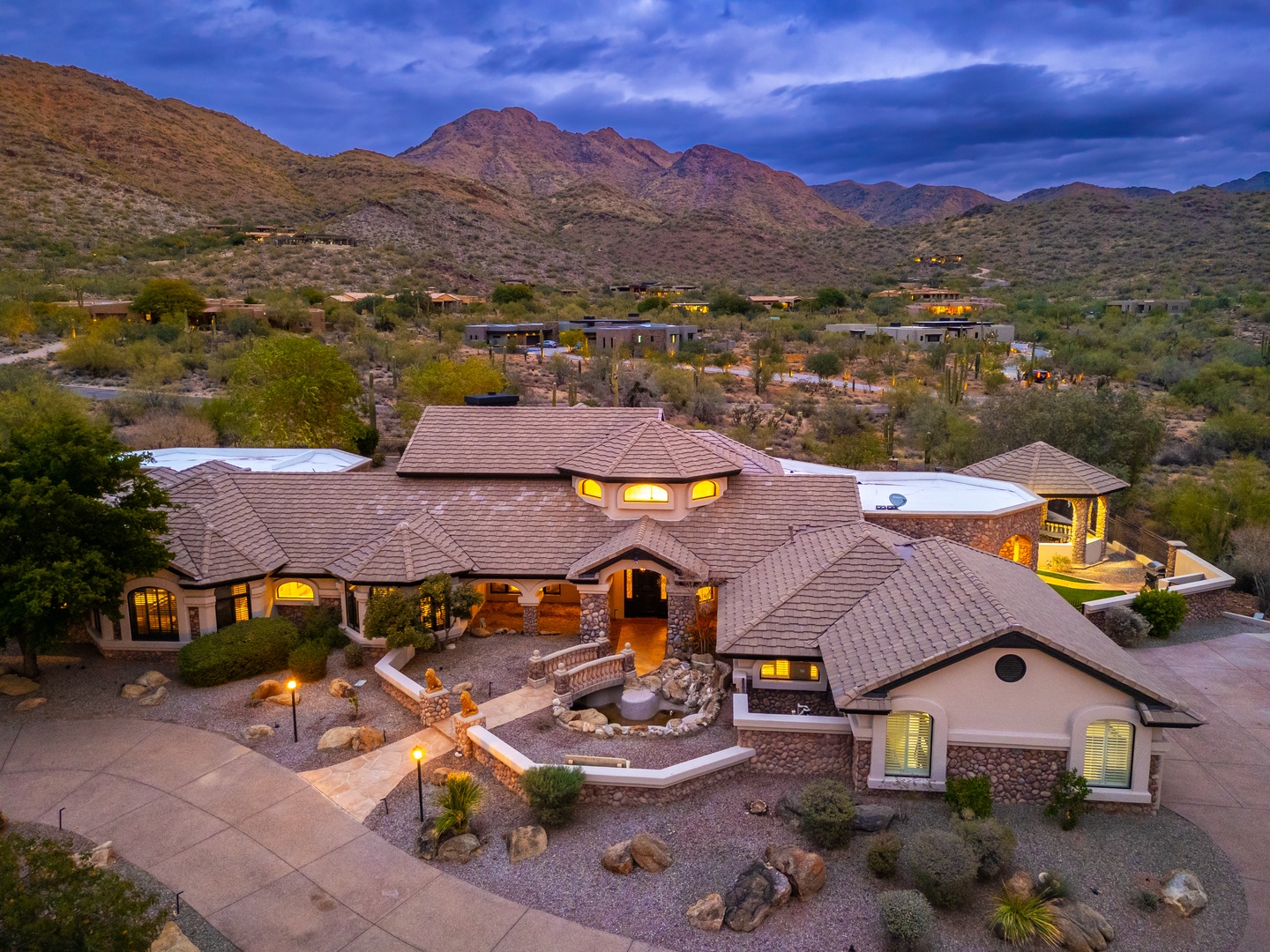 Stunning desert estate nestled against mountain foothills, featuring elegant architecture, inviting outdoor spaces, and surrounded by natural desert landscape and dramatic mountain views.