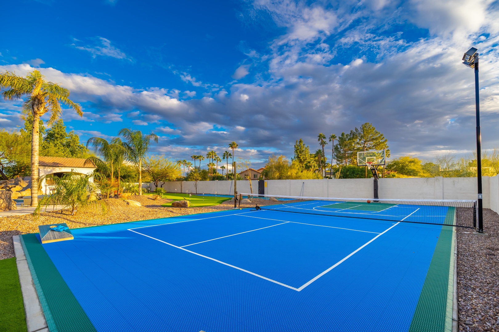 A private tennis court with basketball hoop awaits, surrounded by desert palms and views of the neighboring landscape under sunny skies.